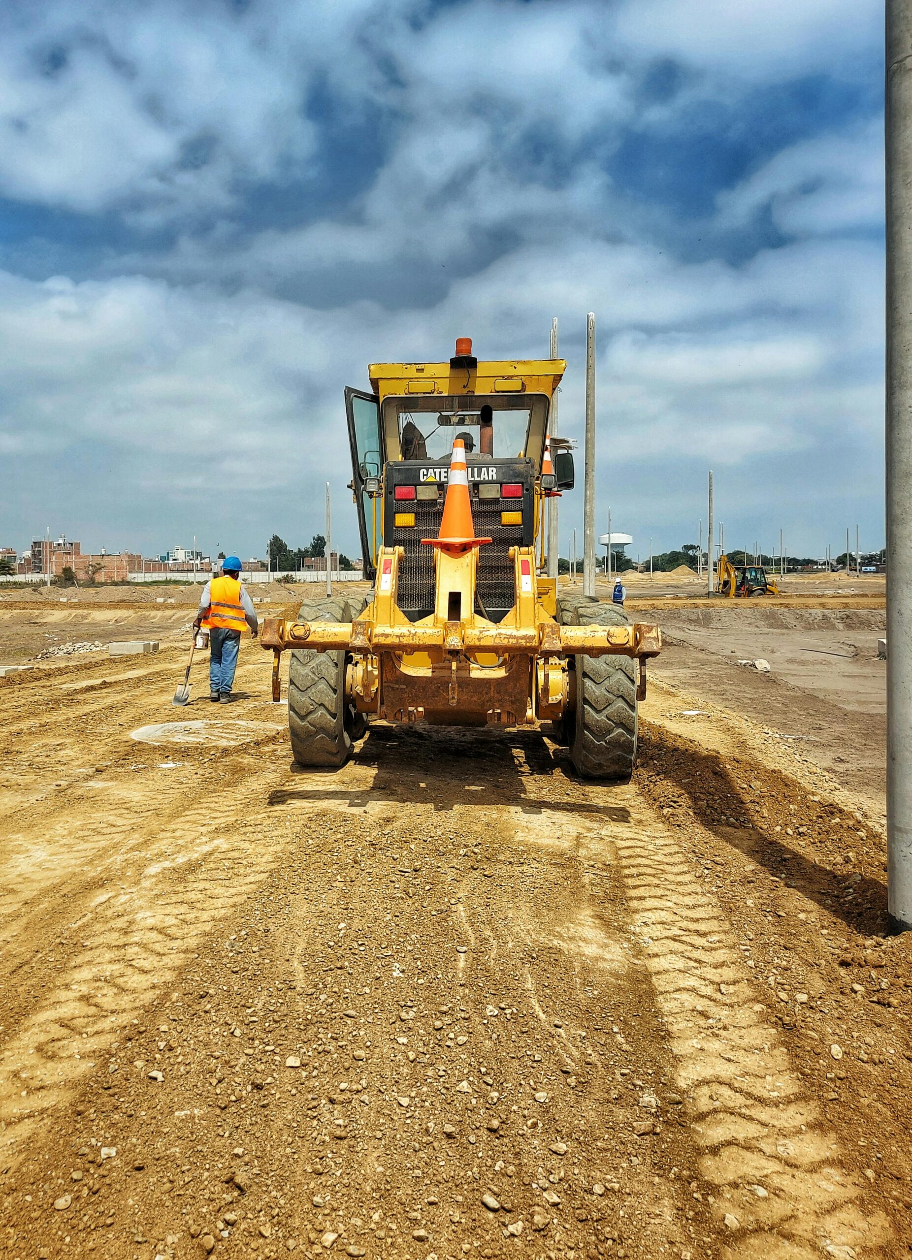 Motor grader on a construction site preparing dirt ground on a sunny day.